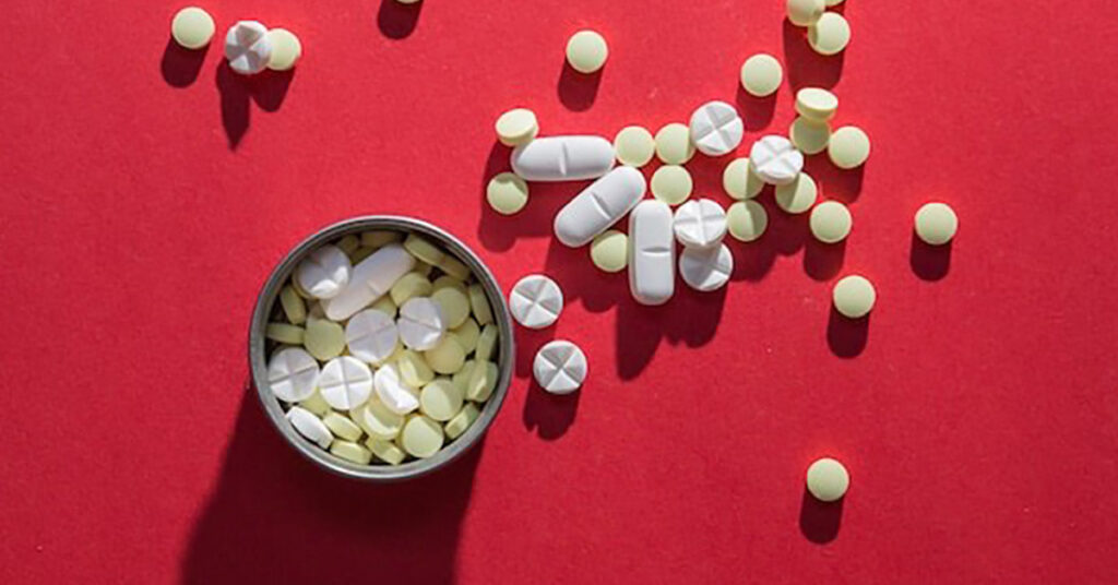 Assorted Tylenol tablets and capsules spilled from container on red background, symbolizing medicine and pain relief.